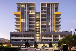 Strathfield apartment building with modern design, twin towers, glass atrium, and yellow highlights at dusk.