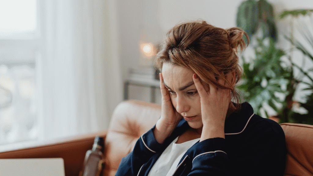 A woman sitting on a couch holding her head in frustration, looking stressed and overwhelmed at home.
